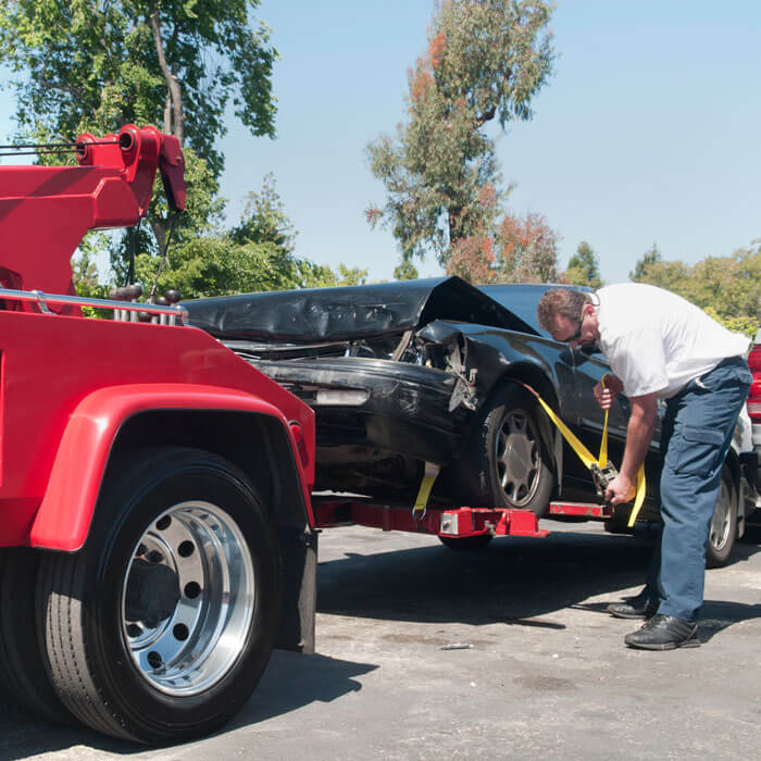 man strapping wrecked car to red tow truck