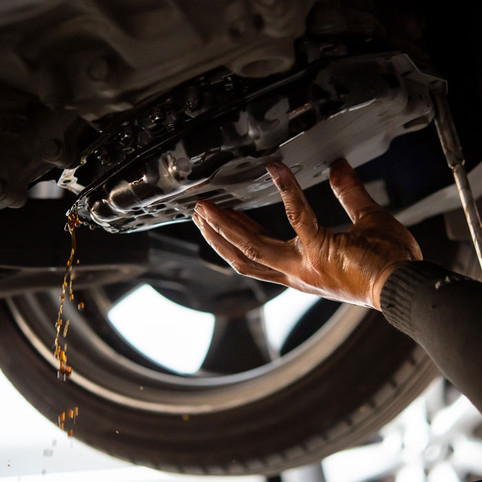 man draining transmission fluid from underneath car