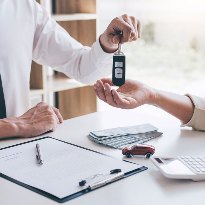 Car salesman holding key of car giving to woman client after signing sale contract